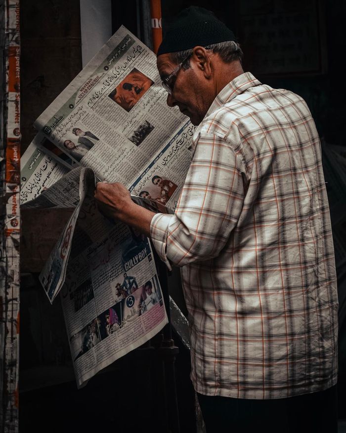why-choose-us Elderly man in plaid shirt engrossed in reading a newspaper indoors.