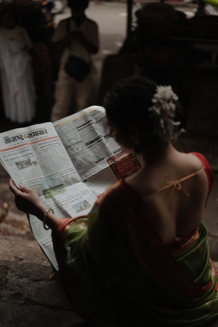 ours-journey A woman in traditional Indian attire reads a newspaper while seated outdoors, capturing a candid moment.