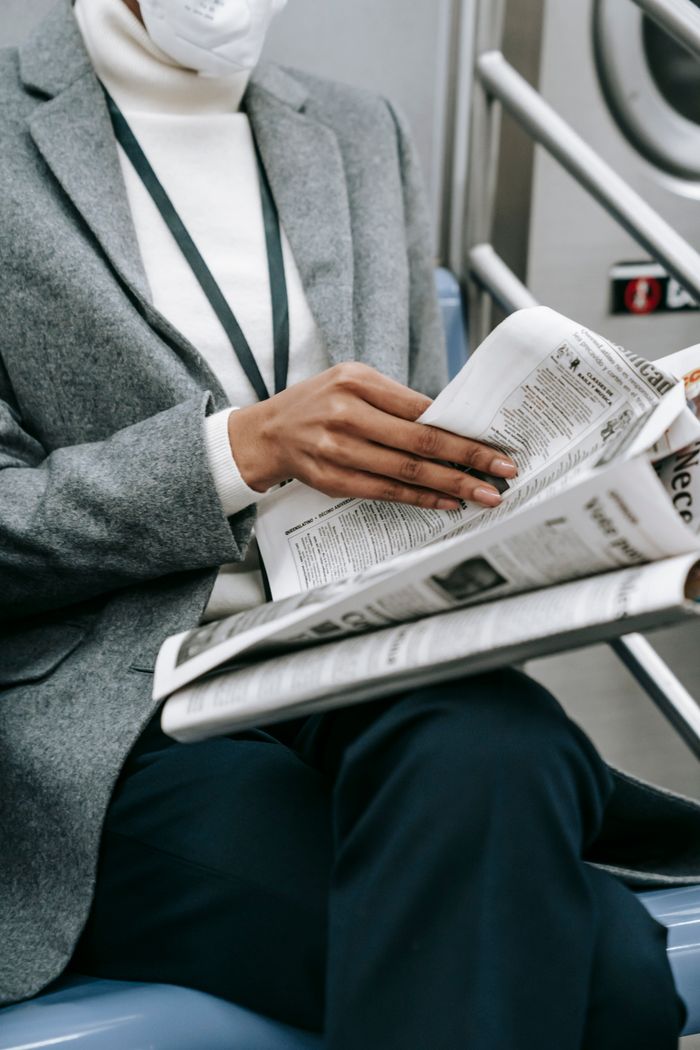 gallery-5 Crop anonymous black female entrepreneur in elegant outfit and medical mask reading newspaper while riding train